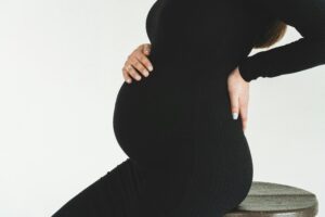 Close-up of a pregnant woman in a black dress holding her back, showcasing her pregnancy bump.